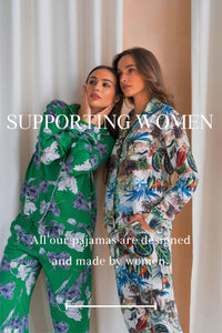 One white woman with her hans on her face wearing green pajamas, leaning against another with woman wearing white pajamas as they look off into the distance. "Supporting Women - All our pajamas are designed and made by women." is the text overlay for the image.